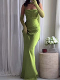 Full front view of a green draped strappy maxi dress worn indoors with long glove styling