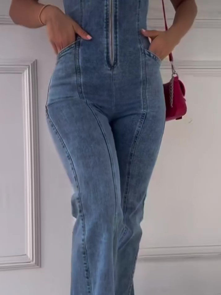 Close front view of a blue denim jumpsuit showing the centre zipper, panel seams and curved front pockets