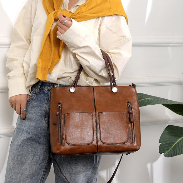 Brown two-handle shoulder bag carried at the hip over a white shirt and jeans.