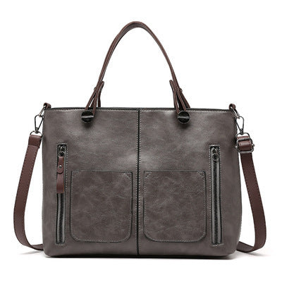 Grey two-handle shoulder bag with front pockets, vertical zippers and a long strap on white.