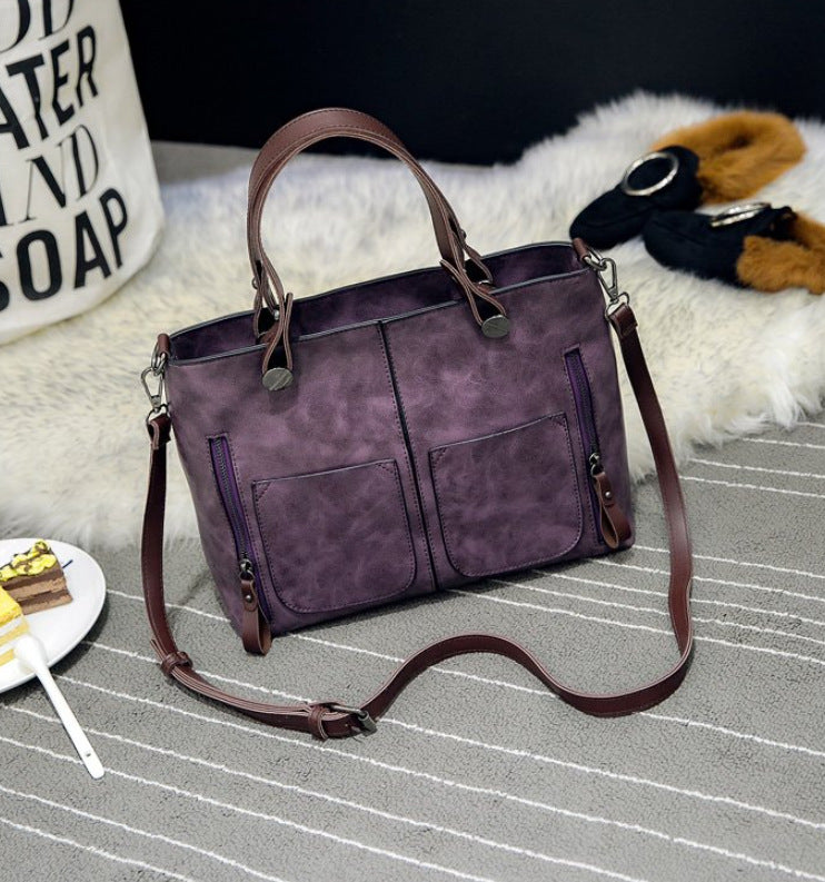Two-handle shoulder bag with a long strap displayed on a striped surface.