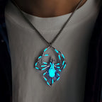 Spider-shaped pendant necklace with blue-green accents, shown worn over a white shirt