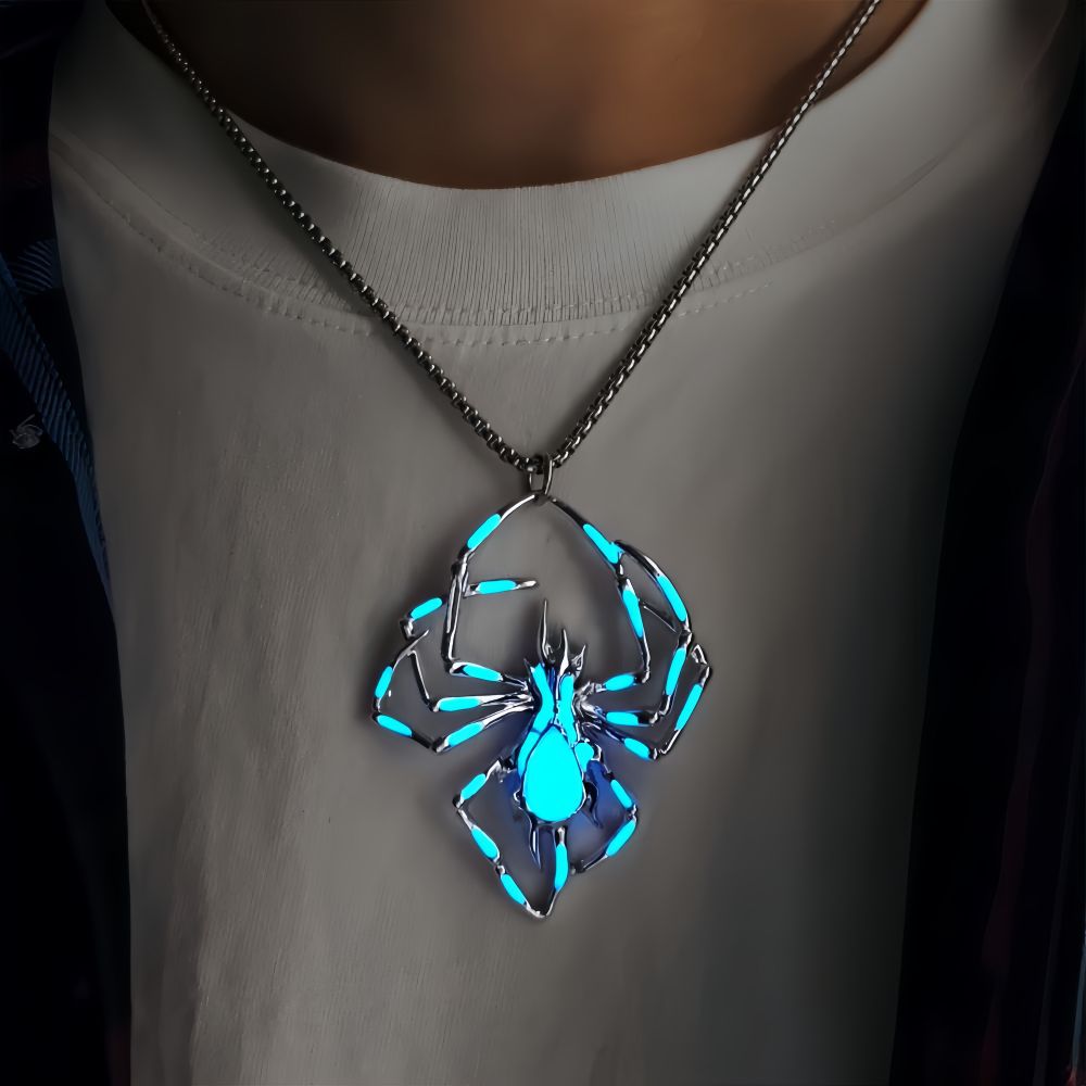 Spider-shaped pendant necklace with blue-green accents, shown worn over a white shirt