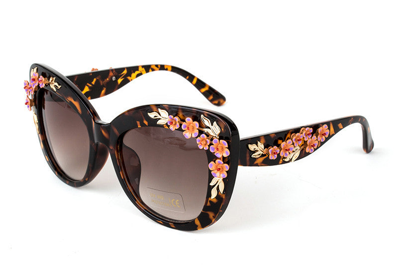One pair of tortoiseshell cat-eye sunglasses with pink flower and gold-tone leaf embellishments on white