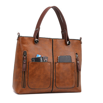 Brown two-handle shoulder bag on white, with small items shown in its front pockets.