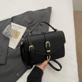 Black handbag with a top handle, shoulder strap and gold-tone clasp, shown held in a hand