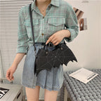 Black bat-wing-shaped crossbody bag worn across a green checked shirt.