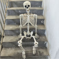 White full-body skeleton decoration seated on concrete steps, with its skull, ribcage, arms, legs and feet visible.