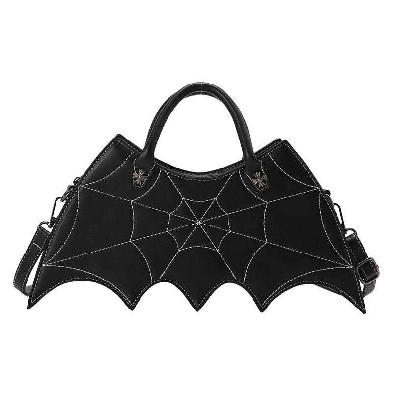 Black bat-wing-shaped crossbody bag with spider-web stitching, two handles and a shoulder strap on white.