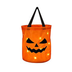 Orange jack-o'-lantern candy bag with a frowning face and black handle, shown with glowing points on white.