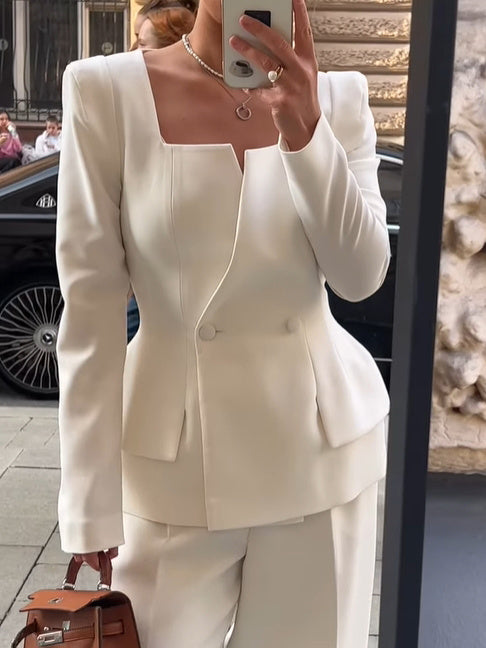 Front view of a white square-neck blazer with covered buttons and a layered hem; trousers and bag are styling accessories