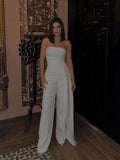 White strapless top and wide-leg trousers worn indoors, showing the long asymmetric side drape.