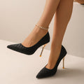 Black pointed-toe pumps with gold-colour heels, shown as a pair worn on feet