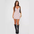 White mini dress with red rose print, thin straps and a front bow, worn — front view