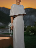 Outdoor front view of a pale fitted dress with a cape-style shoulder overlay