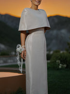 Outdoor front view of a pale fitted dress with a cape-style shoulder overlay