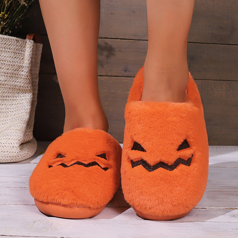 Pair of orange pumpkin-face slippers shown worn from the front