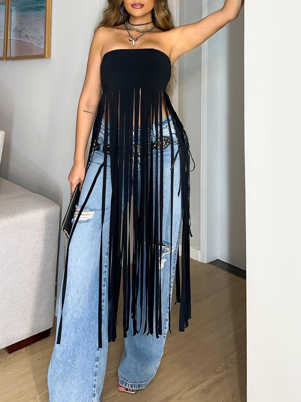 Model wearing a black bandeau top with long fringe over blue jeans