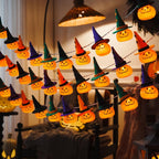 Illuminated pumpkin lights wearing orange, purple, green and black witch hats, displayed in several hanging rows indoors.