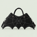 Black bat-wing crossbody bag with web stitching, two handles and strap against pale sage.