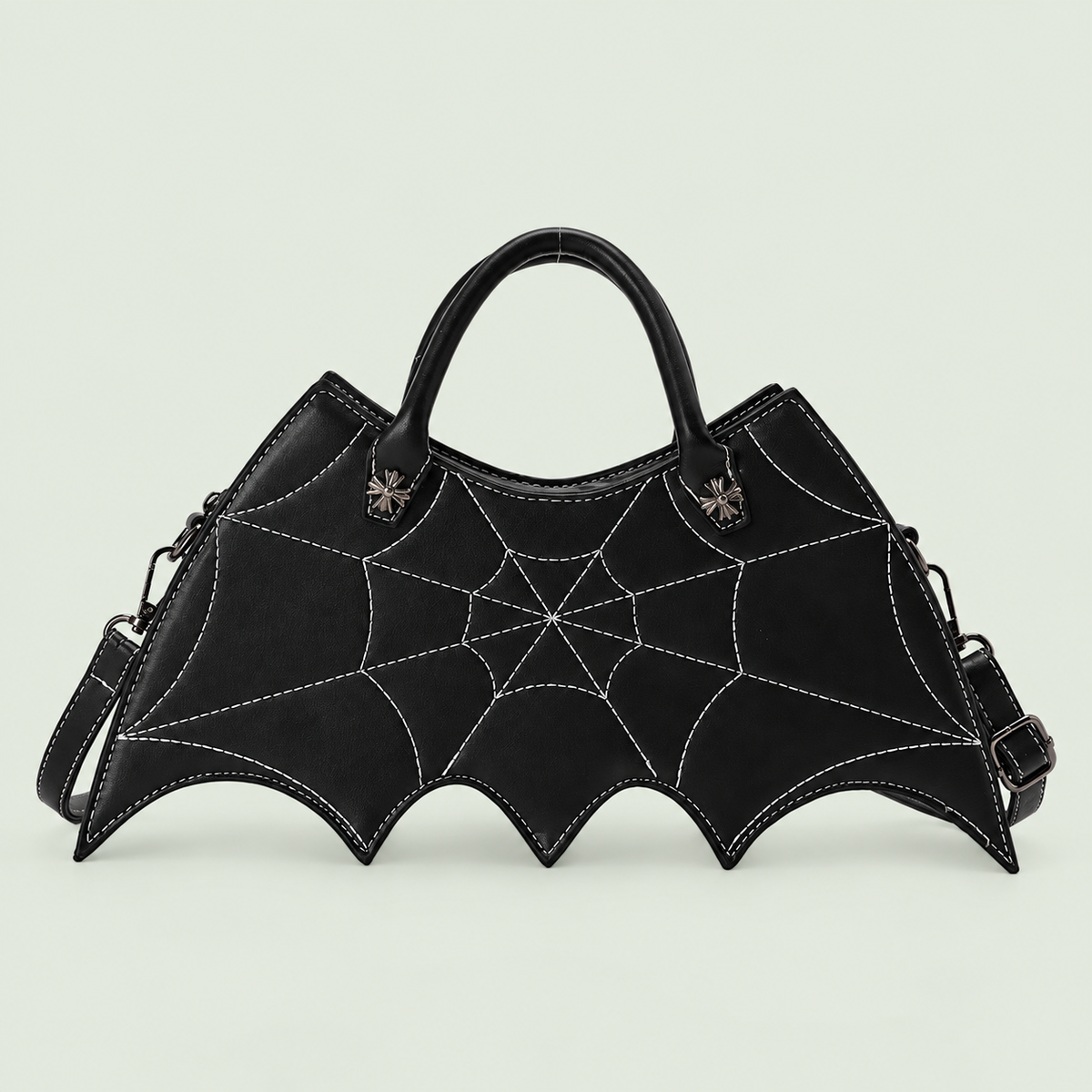 Black bat-wing crossbody bag with web stitching, two handles and strap against pale sage.