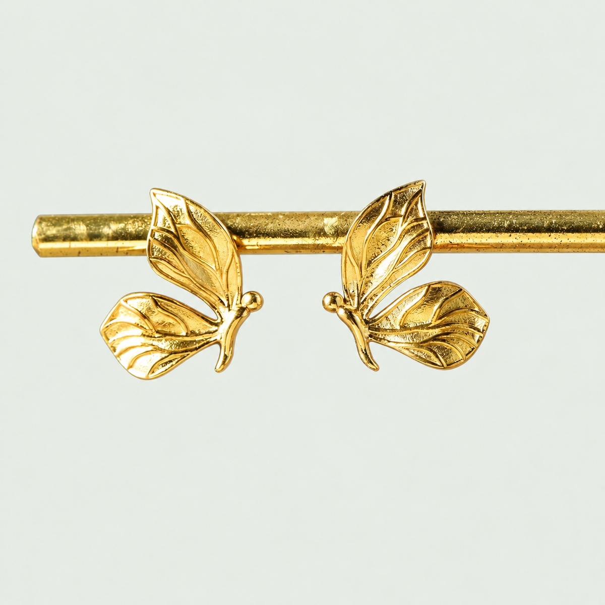 Pair of Butterfly Stud Earrings on their display support against pale sage