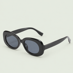 Glossy black oval sunglasses with dark lenses and wide arms against pale sage.