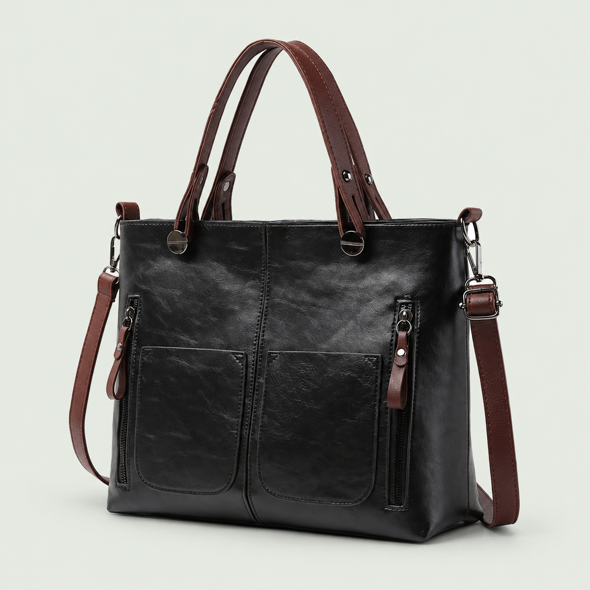 Black shoulder bag with brown handles and strap, two front pockets and vertical zippers against pale sage.